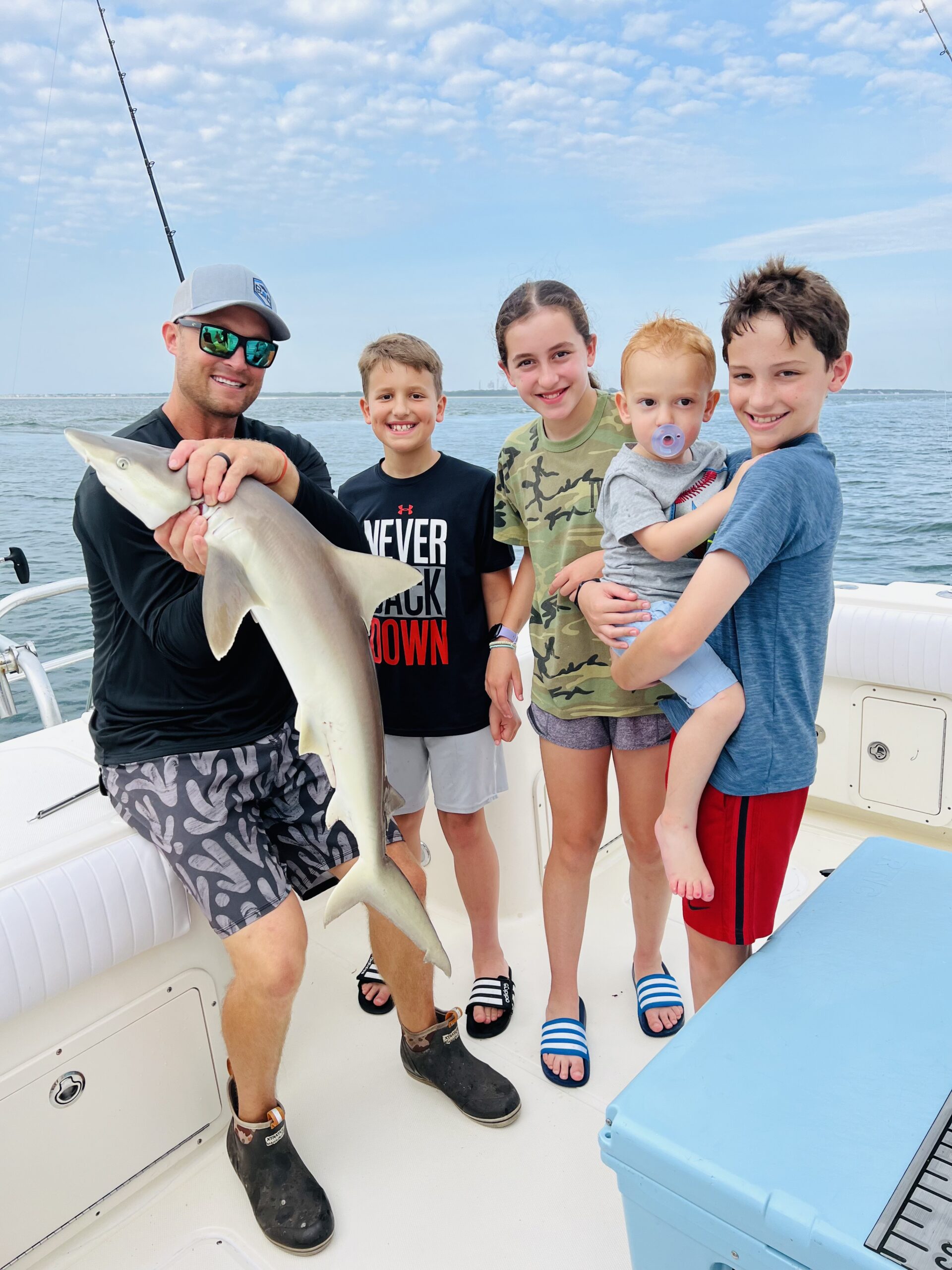 Man and four kids with a small shark catch on a jetty trip